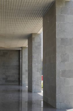 Gri sütunları olan bir binada uzun bir koridor ve sütunların arasından gelen birkaç ışık huzmesi.
