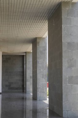 Gri sütunları olan bir binada uzun bir koridor ve sütunların arasından gelen birkaç ışık huzmesi.