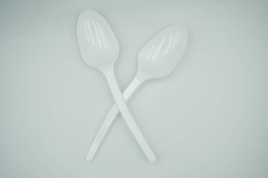 Two white plastic tablespoons curved and stacked crosswise on a white background clipart