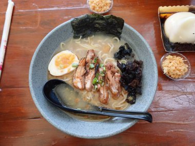Bir kase ramen eriştesi haşlanmış yumurta, yosun örtüsü ve ahşap bir masada tavuk parçaları..