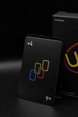 The +4 card is propped up in a black Uno Minimalista playing card box with a black background clipart