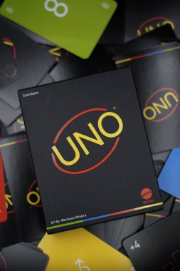 Black Uno Minimalista playing card box among a pile of scattered cards on a black background clipart