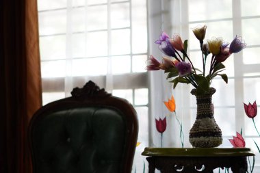 Pencere perdelerinin yanındaki oturma odasındaki masada bir vazo lale sergileniyor.