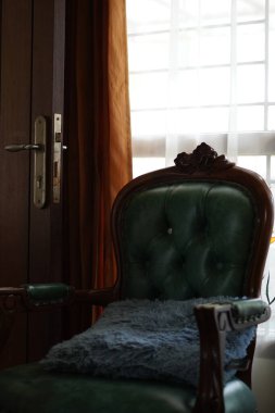 Perdeleri açık, pencerenin yanında yeşil bir sandalye var..