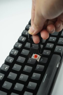 Beyaz arkaplanı olan siyah bir klavyeden tuş kapaklarını çıkaran bir el