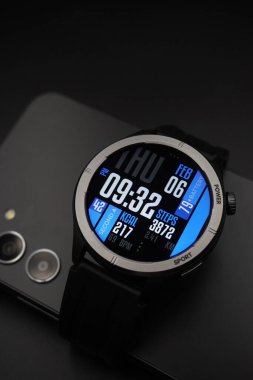 A black smartwatch that is on and displays date and time and health information paired with a smartphone on a black background clipart