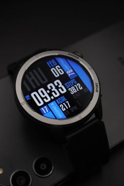 A black smartwatch that is on and displays date and time and health information paired with a smartphone on a black background clipart