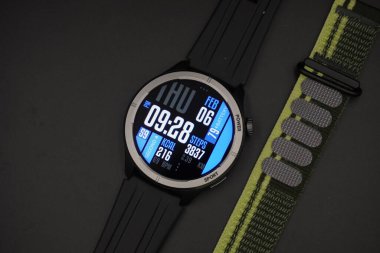 Yanındaki siyah arkaplanlı kumaş kayışıyla aydınlatılmış spor tasarımı olan siyah akıllı saat.