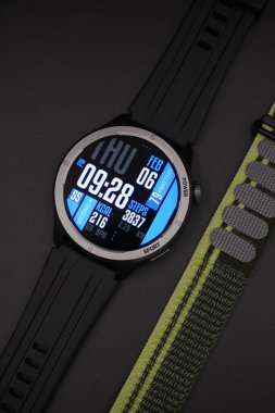Yanındaki siyah arkaplanlı kumaş kayışıyla aydınlatılmış spor tasarımı olan siyah akıllı saat.