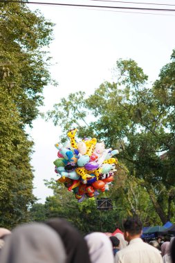 Çocuk karakteri balonları, öğleden sonra ağaçlı bir yerde kalabalığın arasında.