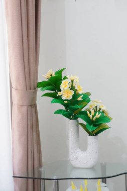Odanın köşesine temiz ve estetik bir dekorasyon olarak yerleştirilmiş eşsiz bir çömleğe yerleştirilmiş yapay frangipani çiçekleri.