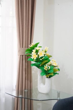 Odanın köşesine temiz ve estetik bir dekorasyon olarak yerleştirilmiş eşsiz bir çömleğe yerleştirilmiş yapay frangipani çiçekleri.