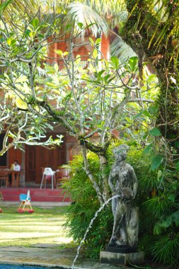 Taştan yapılmış bir kadın heykeli bir sürahi taşıyor ve fıskiyeyi sabah yeşil bahçeli bir havuza boşaltıyor.