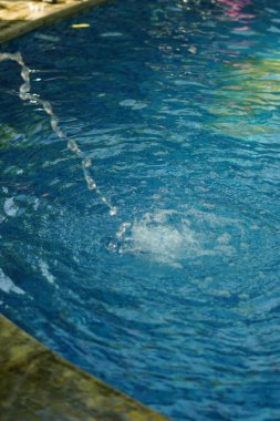 Mavi bir yüzme havuzundaki çeşmeden bir damla su.