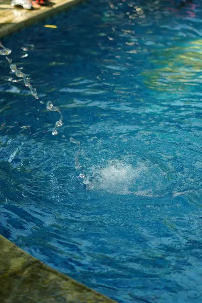 Mavi bir yüzme havuzundaki çeşmeden bir damla su.