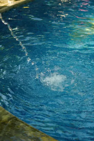 Mavi bir yüzme havuzundaki çeşmeden bir damla su.