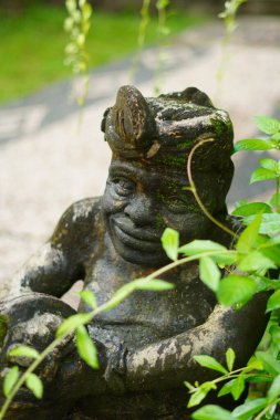 Elinde davul tutan ve çalıların arasında duran Balili bir adamın taş heykeli.