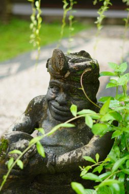 Elinde davul tutan ve çalıların arasında duran Balili bir adamın taş heykeli.