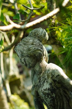 Yeşil bitkilerle oyulmuş taştan yapılmış bir kadın heykeli..