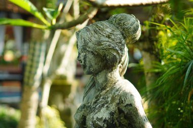 Yeşil bitkilerle oyulmuş taştan yapılmış bir kadın heykeli..