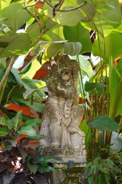 Ağaçların arasında Bali tarzı oymalar yapılmış bir heykel.