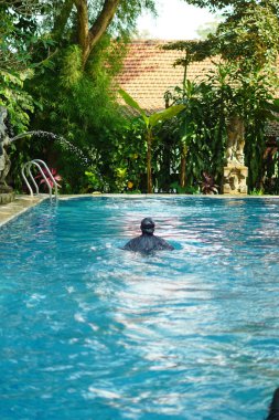Halka açık bir yüzme havuzunda tek başına yüzen tesettürlü bir kadın.