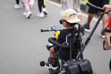Güneş gözlüğü takan ve bebek arabasında oturan bir çocuk ailesi tarafından itiliyor.