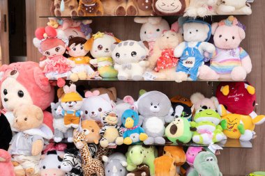 Bir karnavalda açık raflarda gösterilen çeşitli boyut ve karakterlerden oluşan bir oyuncak bebek koleksiyonu.