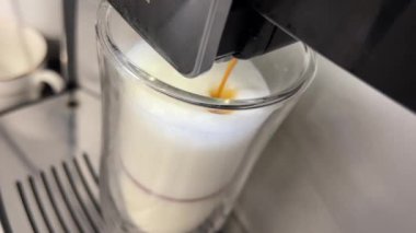 Sütlü cam bardağa dökülen kahveyi yakından çek, otomatik kahve makinesini kullanarak cappuccino yap. Yüksek kalite 4k görüntü