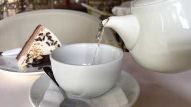 Siyah demlenmiş çay, metal bir çaydanlıktan beyaz bir fincana dökülür. Dolly etkisi. Kapatın. Ağır çekim. Çay takımı bulanık. Yüksek kalite 4k görüntü