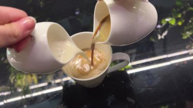 Bir fincan siyah çaya süt ekliyorum. Beyaz ve kahverengi kıvrımlı. - Yakın çekim. Ağır çekim. Döndürme. Soyut kaotik hareket. Krema ve kahveyi aynı anda bir fincana dök.