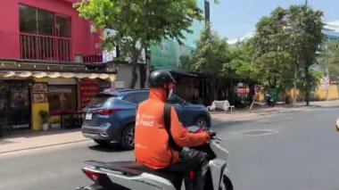 Ho Chi Minh City 'den yiyecek teslimatı, markalı turuncu ceketli bir motosikletçi teslimat yapıyor. Şehirdeki gerçek hayat. Vietnam Ho Chi Minh Şehri 05.11.2024 