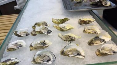 Güzel dekore edilmiş yemek masası istiridye, midye ve deniz ürünleriyle. Kadın elleri buzda istiridye serer, açık büfede istiridye haşlar.