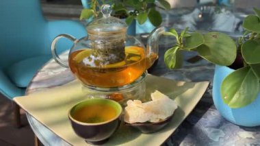 Çay takımı, cam çaydanlık ve fincanlar. Bira. Yavaş çekim çayı. kompozisyon. Yeşil otelin yeşil çayı yasemin çaydanlığı iki fincana doluyor verandada, çiçek saksılarının üzerinde. Güzellik Yasemin