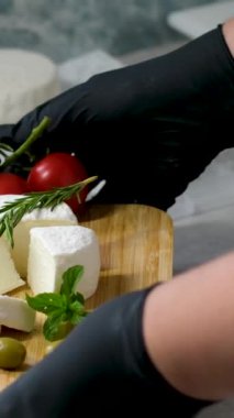 Siyah eldivenli kadın elleri picadon peyniri taşır ünlü Fransız keçi peyniri mükemmel tat ve aroma. Domatesli ahşap kesim tahtası peyniri. Taze bitkiler.