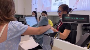 Vietnam 'da bir mağaza, Avrupalı bir kız kasada kıyafet seçiyor, Asyalı ve çok uluslu kadınlar, erkekler kıyafet alıyor, kasiyer makbuz veriyor, Vietnam Ho Chi Minh City 05.11.2024