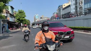 Vietnam motosikleti bir arabayı sollar. En iyi ulaşım motosikletçisi iki parmak Victory 'i gösterir. Vietnam Ho Chi Minh Şehri 05.28.2024 