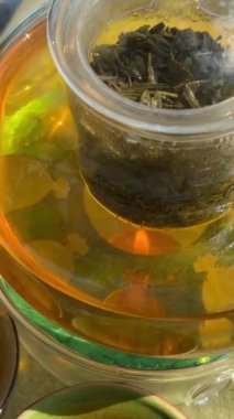 Taze çiğ yeşil çay yaprağı tomurcuğu limon portakal, şeffaf cam çay fincanı çay fincanı, beyaz arka plan manzaralı pan zoom üzerinde döner. Yüksek kalite 4k görüntü