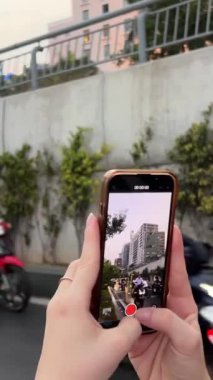 Avrupalı turist, Vietnam 'da yol boyunca seyahat eden motosikletlerin fotoğraflarını cep telefonuyla çekiyor. Vietnam Ho Chi Minh Şehri 05.27.2024