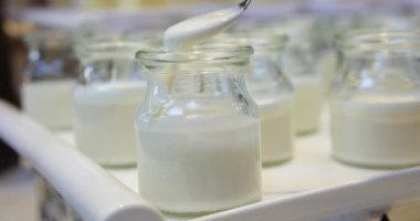 Masada bir kavanoz yoğurt, süt ve krema var. Süt bir bardağa ve bir kavanoza kaşık kullanılarak dökülür. Orada bir bardak daha süt var. Yüksek kaliteli FullHD görüntüler