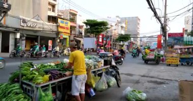 Fakir bir adam alışveriş arabasıyla yeşil otlarla şehir merkezinde soğanlı kişniş satar Saigon Vietnam yolunda 02.09.2024
