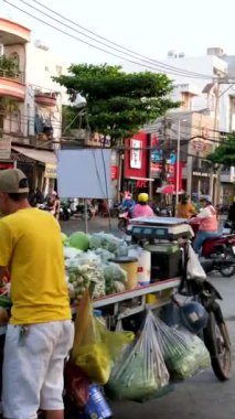 Fakir bir adam alışveriş arabasıyla yeşil otlarla şehir merkezinde soğanlı kişniş satar Saigon Vietnam yolunda 02.09.2024