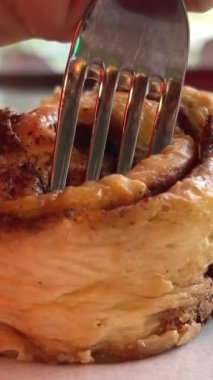 Kadın eli bir tabak günahı döndürür. Kremalı kıvırcık kek. Yakın çekim, ön manzara. Cinnabon. Kuru tarçınlı rulo. Restoranda çatal ve bıçakla kesilmiş. Taze tatlı değil.