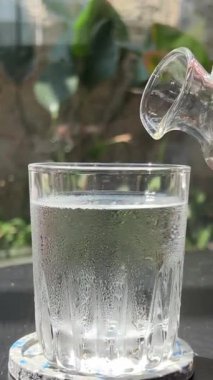 Masanın üzerine bir bardak su dökün. Bir insanın elindeki küçük bir sürahi daha kalın bir sıvı karışımı bir topinaya dökün. Yüksek kalite 4k görüntü