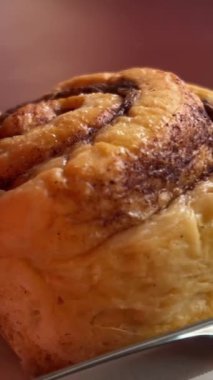 Kadın eli bir tabak günahı döndürür. Kremalı kıvırcık kek. Yakın çekim, ön manzara. Cinnabon. Kuru tarçınlı rulo. Restoranda çatal ve bıçakla kesilmiş. Taze tatlı değil.