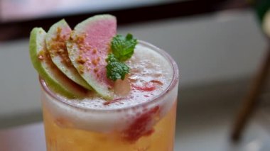 Kırmızı guava suyu ağacın arka planında bulanık bir bardağa dökülüyor. Meyve suyu hazırlanıyor. Ağır çekim. Yüksek kalite 4k görüntü