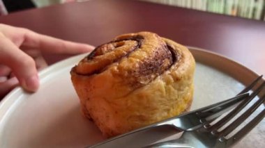 Kadın eli bir tabak günahı döndürür. Kremalı kıvırcık kek. Yakın çekim, ön manzara. Cinnabon. Kuru tarçınlı rulo. Restoranda çatal ve bıçakla kesilmiş. Taze tatlı değil.