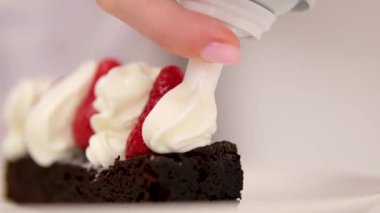 Çikolatalı Brownie, çilekli ve kremalı. Çilekleri kremayla süsleyin. Çileklerin üzerine krema döken çikolatalı brownie tatlısından leziz yemekler.