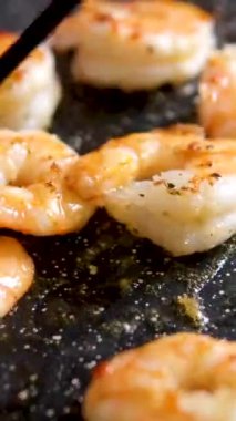 Profesyonel şef karidesleri siyah tavada pişirir ve restoran mutfağında zeytinyağı ile pişirir. Lezzetli deniz ürünleri pişirme teması. Akıllı telefonlar için dikey video. sosyal medyada tabletler.