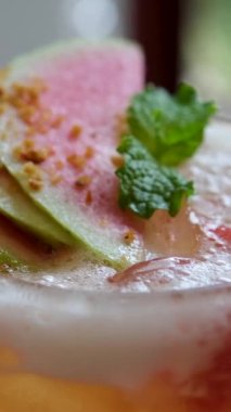 Yakın plan çekimde, taze guava suyunu bardakla gözlüyor ve naneli yapraklarla süslüyor. Yüksek kalite 4k görüntü